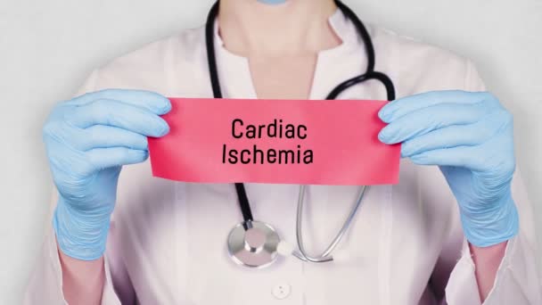 Gros plan, les mains en gants médicaux bleus tiennent et déchirent carton rouge avec une inscription Ischémie cardiaque. médecin habillé en uniforme médical blanc, a un stéthoscope . — Video