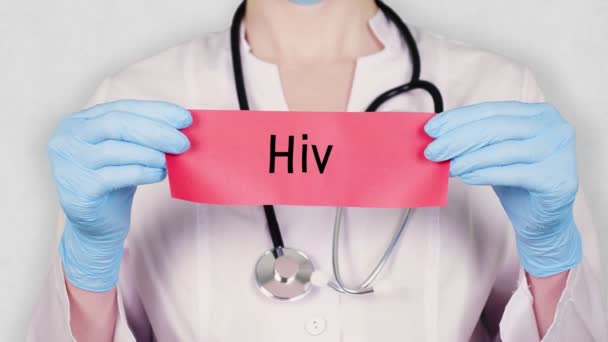 Closeup, τα χέρια σε μπλε ιατρικά γάντια κρατήστε και δάκρυ κόκκινη κάρτα χαρτί με μια επιγραφή hiv. γιατρός ντυμένος με λευκή ιατρική στολή, έχει στηθοσκόπιο. — Αρχείο Βίντεο