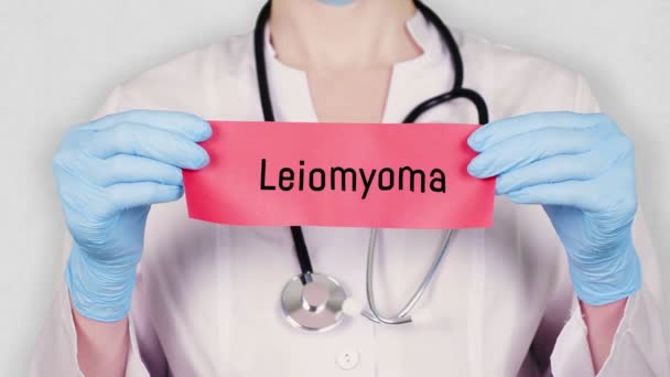 Крупный план, руки в синих медицинских перчатках держат и рвут красную бумажную карточку с надписью лейомиома. врач в белой медицинской форме, имеет стетоскоп . — стоковое видео