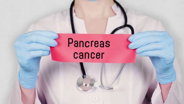 Primo piano, mani in guanti medici blu tenere e strappare carta di carta rossa con un'iscrizione cancro al pancreas. medico vestito in uniforme medica bianca, ha uno stetoscopio . — Video Stock