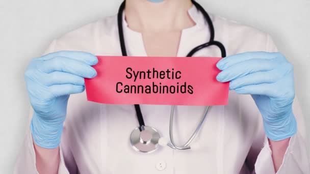 Gros plan, les mains en gants médicaux bleus tiennent et déchirent le carton rouge avec une inscription cannabinoïdes synthétiques. médecin vêtu d'uniforme médical blanc, stéthoscope . — Video