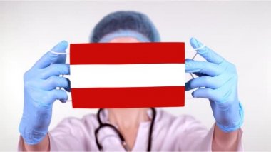 Yakın plan. Gözlüklü doktor, mavi tıbbi şapkalı, eldivenli Avusturya bayrağı ile tıbbi maske takıyor. Doktorlar, koronavirüs sırasında devletin koruması, küresel salgın. Kavram.