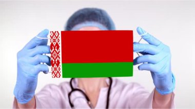 Yakın plan. Gözlüklü doktor, mavi tıbbi şapkalı, eldivenleri elinde. Beyaz Rusya bayrağıyla tıbbi maske takıyor. Doktorlar, koronavirüs sırasında devletin koruması, küresel salgın. Kavram.
