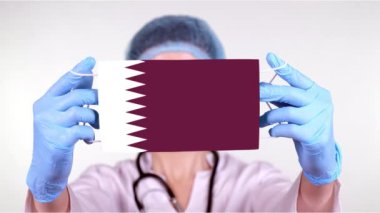 Yakın plan. Gözlüklü doktor, mavi tıbbi şapkalı, eldivenli Katar bayrağıyla tıbbi maske takıyor. Doktorlar, koronavirüs sırasında devletin koruması, küresel salgın. Kavram.