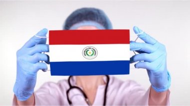 Yakın plan. Gözlüklü doktor, mavi tıbbi şapkalı, eldivenli, Paraguay bayrağıyla tıbbi maske takıyor. Doktorlar, koronavirüs sırasında devletin koruması, küresel salgın. Kavram.
