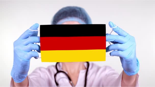 Detailní záběr. Doktor v brýlích, modrý lékařský uzávěr, rukavice v rukou, lékařská maska s německou vlajkou. Lékaři pečují, chrání stát během koronaviru, globální epidemie. Koncept. — Stock video