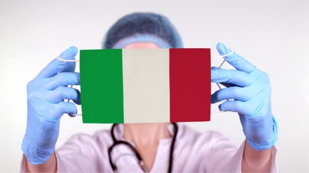 特写。戴眼镜的医生，戴着蓝色的医疗帽，戴着手套，戴着印有意大利国旗的医疗面罩。医生关心，在验尸官出现时受到国家的保护，全球性的流行病。概念. — 图库视频影像