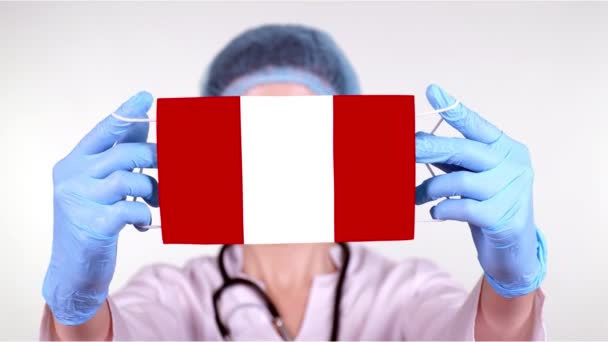 Närbild. Läkare i glasögon, blå medicinsk mössa, handskar håller i händerna medicinsk mask med Peru flagga. Läkarvård, skydd efter stat under coronavirus, global epidemi. Begreppet. — Stockvideo