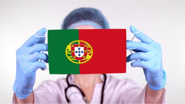 Yakın plan. Gözlüklü doktor, mavi tıbbi şapkalı, eldivenli, Portekiz bayrağıyla tıbbi maske takıyor. Doktorlar, koronavirüs sırasında devletin koruması, küresel salgın. Kavram. — Stok video