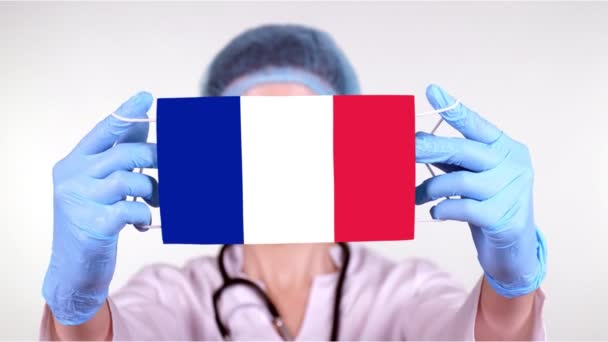 Close-up. Doctor in glasses, blue medical cap, gloves holds in hands medical mask with France flag. Physicians care, protection by state during coronavirus, global epidemic. Concept. — Stock Video