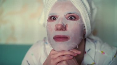 yakın plan, portre, kozmetik kumaş maskeli bir kadın ve kafasında beyaz bir havluyla, geceleri korku filmi izleyen bir kadın..