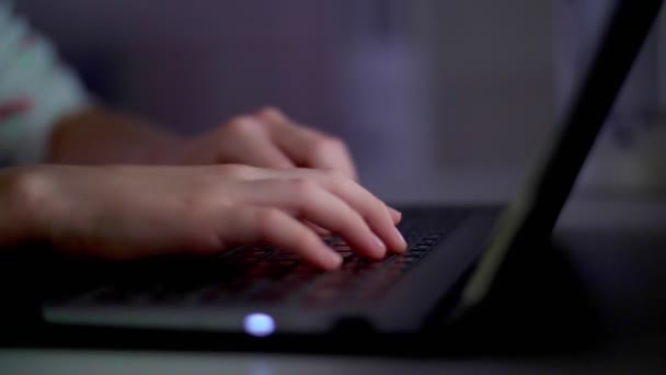 Primo piano, le mani di una ragazza, un bambino stanno digitando su una tastiera del computer portatile, sotto la luce del monitor, di notte . — Video Stock