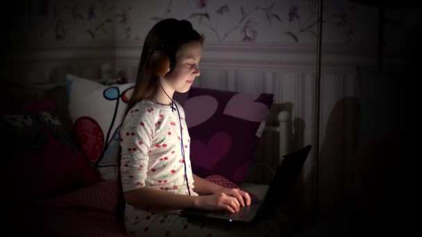 Adolescente, in pigiama, in cuffia, guardando qualcosa su un computer portatile, tipi, ascolta la musica, di notte, in camera da letto. bambino, adolescente lavora sul computer portatile di notte — Video Stock