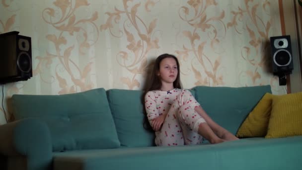 Adolescente en pyjama regardant un film à la télé dans l'obscurité, assise sur le canapé. La pièce est éclairée par la lumière de l'écran de télévision . — Video