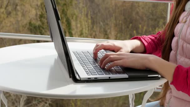 Zbliżenie rąk wpisujących na klawiaturze laptopa. nastolatka pisze, pracuje na laptopie, na otwartym balkonie. wiosenny słoneczny dzień. — Wideo stockowe