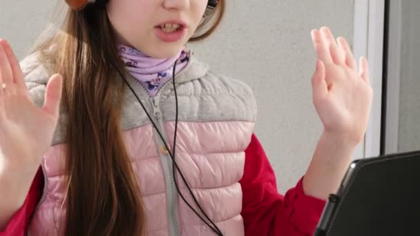 Tiener meisje in koptelefoon, werkt op laptop, chatten online, op een open balkon. Zonnige lentedag. Afstandsonderwijs. quarantaine. Blijf, studeer thuis. Coronavirusepidemie. — Stockvideo