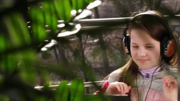 Adolescente ragazza in cuffia, lavorando sul computer portatile, chattando online, sul balcone aperto. giornata di sole primaverile. Imparare a distanza. quarantena. Resta, studia a casa. epidemia di coronavirus . — Video Stock