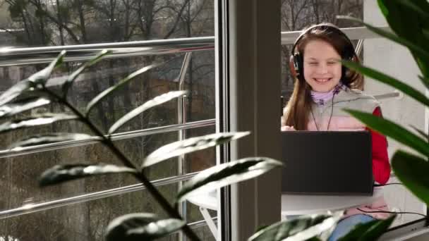 Дівчина-підліток в навушниках, слухає музику на ноутбуці, спілкується онлайн, на відкритому балконі. весняний сонячний день. карантин. залишатися, вчитися вдома. епідемія коронавірусу . — стокове відео