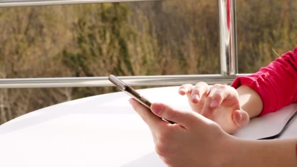 Primer plano de las manos, chica adolescente utiliza teléfono inteligente, en el balcón abierto. Primavera día soleado . — Vídeos de Stock