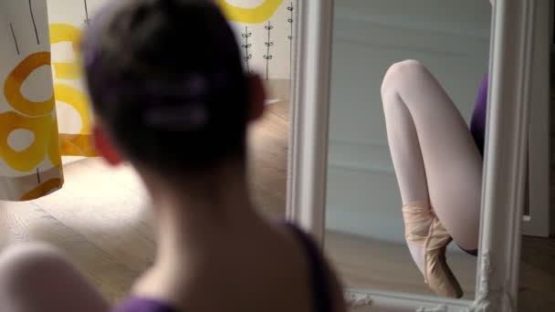 Молодой балетный танцор выполняет пуанты упражнения, сидя на полу. Девочка-подросток растягивает ноги. ее ноги в пуантах отражаются в зеркале — стоковое видео