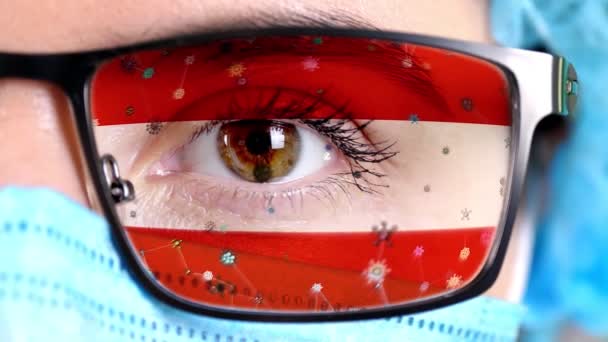 Close-up, oog, deel van de arts gezicht in medisch masker, bril, die geschilderd in de kleuren van Oostenrijk vlag. Veel virussen, ziektekiemen bewegen zich op glas. Staatsbelangen in vaccins, medicijnen uitvinding, pathogene — Stockvideo