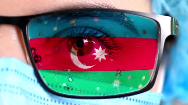 Primer plano, ojo, parte de la cara del médico en máscara médica, gafas, que pintó en colores de la bandera de Azerbaiyán. Muchos virus, gérmenes que se mueven sobre el vidrio.Intereses estatales en las vacunas, la invención de medicamentos, patógenos — Vídeos de Stock