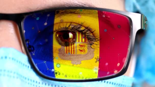 Closeup, eye, part of doctor face in medical mask, glasses, which painted in colors of Andorra flag. Many viruses, germs moving on glass.State interests in vaccines, drugs invention, pathogenic — Stock Video