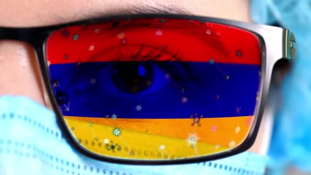 Closeup, eye, part of doctor face in medical mask, glasses, which painted in colors of Armenia flag. Many viruses, germs moving on glass.State interests in vaccines, drugs invention, pathogenic — Stock Video