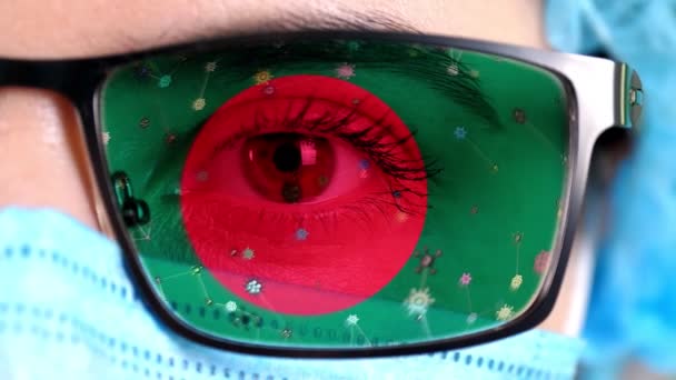 Nahaufnahme, Auge, Teil des Arztgesichts in medizinischer Maske, Brille, die in den Farben der Flagge Bangladeschs bemalt ist. Viele Viren, Keime, die sich auf Gläsern bewegen. Staatliches Interesse an Impfstoffen, Arzneimittelerfindungen, pathogenen — Stockvideo