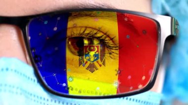 Yakın plan, göz, tıbbi maskeli doktor yüzünün bir parçası, Moldova bayrağının renklerine boyanmış gözlük. Birçok virüs, camlarda hareket eden mikroplar. Aşılara, uyuşturucu icatlarına, patojenik ilaçlara devletin ilgisi.