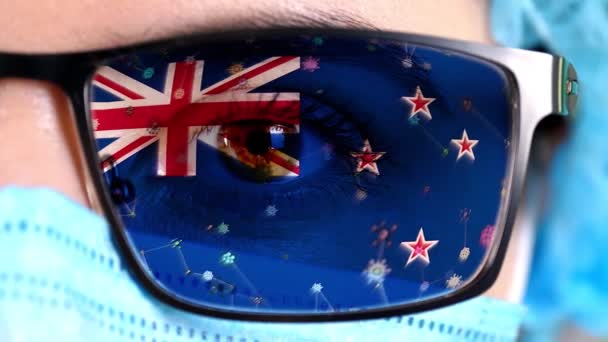 Closeup, eye, part of doctor face in medical mask, glasses, which painted in colors of New Zealand flag. Many viruses, germs moving on glass.State interests in vaccines, drugs invention, pathogenic — Stock Video