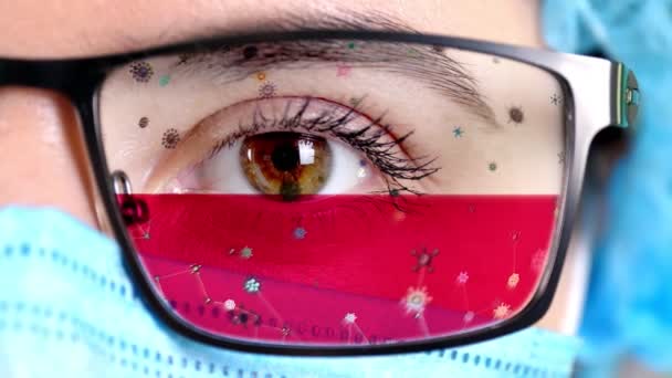 Detailní záběr, oko, část lékařského obličeje v lékařské masce, brýle, které malují v barvách polské vlajky. Mnoho virů, bakterií pohybujících se na skle.Státní zájmy ve vakcínách, vynálezy léků, patogenní viry — Stock video