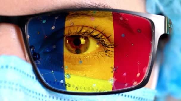 Närbild, öga, en del av läkare ansikte i medicinsk mask, glasögon, som målade i färger i Rumänien flagga. Många virus, bakterier som rör sig på glas.Statliga intressen i vacciner, droger uppfinning, patogena — Stockvideo