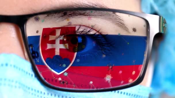 Primer plano, ojo, parte de la cara del médico en máscara médica, gafas, que pintó en colores de la bandera de Eslovaquia. Muchos virus, gérmenes que se mueven sobre el vidrio.Intereses estatales en las vacunas, la invención de medicamentos, patógenos — Vídeo de stock