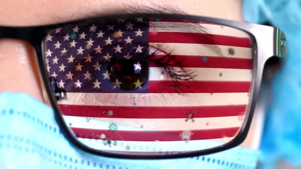 Närbild, öga, en del av läkare ansikte i medicinsk mask, glasögon, som målade i färger av USA flagga. Många virus, bakterier som rör sig på glas.Statliga intressen i vacciner, läkemedelsuppfinningar, patogena virus — Stockvideo