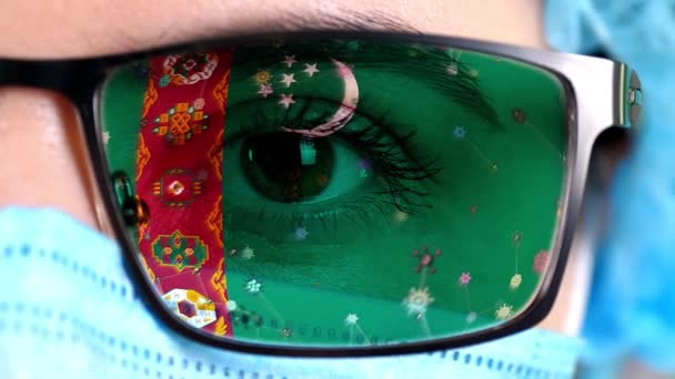 Primer plano, ojo, parte de la cara del médico en máscara médica, gafas, que pintó en colores de la bandera de Turkmenistán. Muchos virus, gérmenes que se mueven sobre el vidrio.Intereses estatales en las vacunas, la invención de medicamentos, patógenos — Vídeo de stock