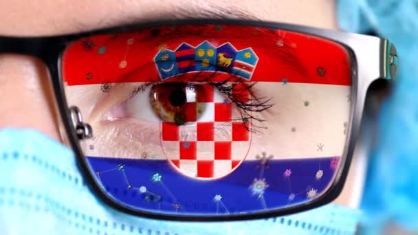 Primer plano, ojo, parte de la cara del médico en máscara médica, gafas, que pintó en colores de la bandera de Croacia. Muchos virus, gérmenes que se mueven sobre el vidrio.Intereses estatales en las vacunas, la invención de medicamentos, patógenos — Vídeo de stock
