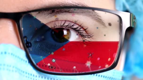 Primer plano, ojo, parte de la cara del médico en máscara médica, gafas, que pintó en colores de la bandera de la República Checa. Muchos virus, gérmenes que se mueven sobre el vidrio.Intereses estatales en las vacunas, la invención de medicamentos, patógenos — Vídeo de stock