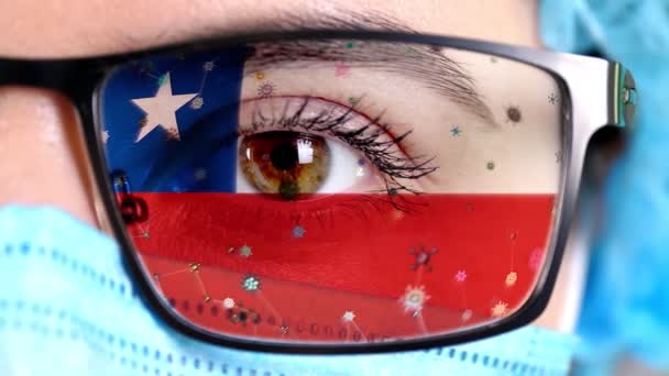 Close-up, oog, deel van de arts gezicht in medische masker, bril, die geschilderd in de kleuren van Chili vlag. Veel virussen, ziektekiemen bewegen zich op glas. Staat belangen in vaccins, medicijnen uitvinding, pathogene virussen — Stockvideo