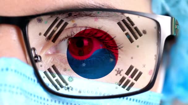 Closeup, eye, part of doctor face in medical mask, glasses, which painted in colors of South Korea flag. Many viruses, germs moving on glass.State interests in vaccines, drugs invention, pathogenic — Stock Video