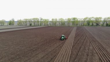 Havacılık. Bahar güneşli bir gün. Tarımsal bir tarlada traktör toprak ve toprak sürüyor. Çiftliklerde otomatik patates ekimi. Modern tarım. Eko çiftliği.