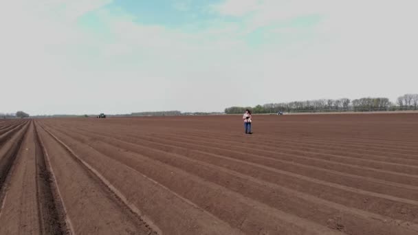 아레로. 농학자인 암컷 농부는 특별 한 토양을 가지고 논에 있다. 그녀는 태블릿을 사용하여 트랙터가 심는 자동화 포 타토의 품질을 테스트 한다. 현대 농업, 농업. 화창 한 봄날. — 비디오
