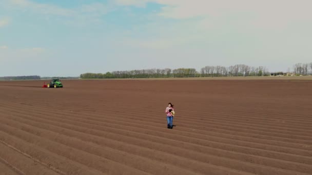 Aero. Kobieta rolnik, rolnik jest na polu ze specjalnymi rzędami gleby. Testuje, używając tabletu, jakość zautomatyzowanego sadzenia ziemniaków przez ciągniki. Nowoczesne rolnictwo, rolnictwo. wiosenny słoneczny dzień. — Wideo stockowe