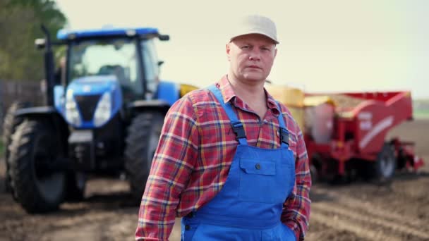 农民或农学家的肖像，穿着红色格子花衬衫，背靠拖拉机、农业机械。现代农业，农业。温暖的晴天 — 图库视频影像