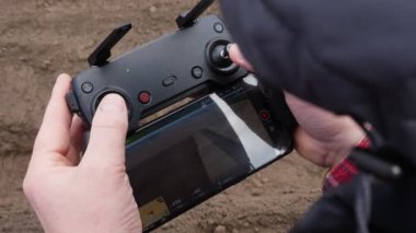 Yakın plan, adam uzaktan kumandayla uzaktan kumandayı tutuyor, traktörün tarlada çalıştığını videoya çekiyor. Tarımsal olarak patates yetiştirme, ekme. Modern tarım. Eko çiftliği. bahar.