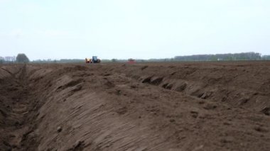 Yakın plan, tarlada kahverengi toprak. Yakınlarda, traktör çalışıyor, toprağı sürüyor, patates ekiyor. Tarımsal olarak patates yetiştiriciliği. Modern tarım. Eko çiftliği. bahar.