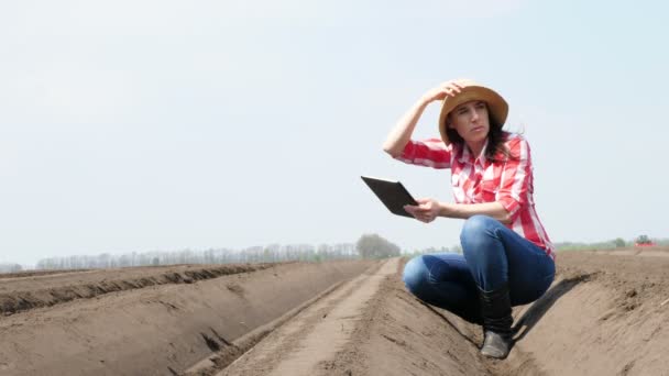 Zemědělka, agronomka, sedí mezi speciálními řadami půdy na poli. Testuje pomocí tabletu kvalitu sadby brambor pomocí kultivátoru. Moderní zemědělství pěstování brambor. jarní slunečný den. — Stock video