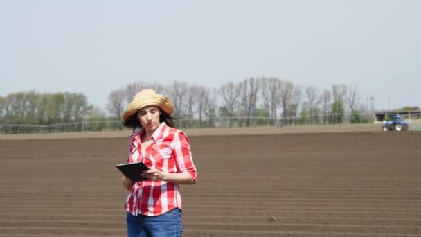 Female farmer, agronomist stands between special soil rows on field. She tests, using tablet, quality of potatoe planting by cultivator. Modern Agriculturally cultivation. spring sunny day. — Stock Video