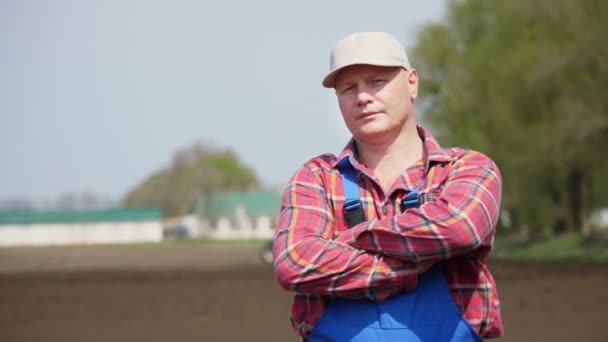 Retrato de agricultor o agrónomo, en camisa a cuadros roja, sobre fondo de tractor de trabajo, cultivador, maquinaria agrícola. agricultura moderna, día soleado de primavera — Vídeo de stock