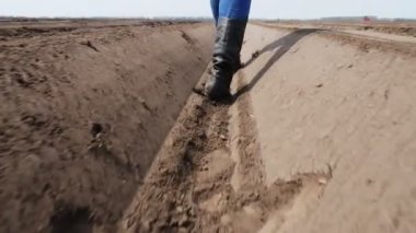 Yakın plan, dişi çiftçi tarlada toprak sıraları arasında, tabletle, tarım vasıtasıyla patates ekiminin kalitesini test ederek derin bir çizgide yürüyor. Modern tarım. Bahar güneşli gün.